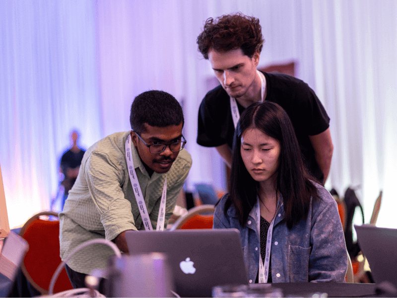 Three hackathon participants collaborating and brainstorming solutions while looking at a laptop.