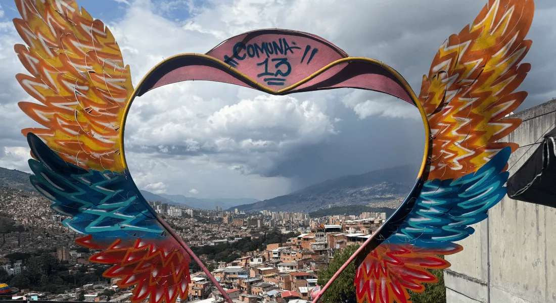 A heart-with-wings sculpture frames a city skyline in the background.