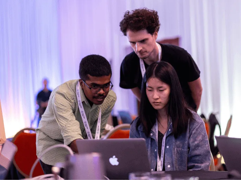 Three hackathon participants collaborating and brainstorming solutions while looking at a laptop.