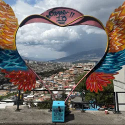 A heart-with-wings sculpture frames a city skyline in the background.