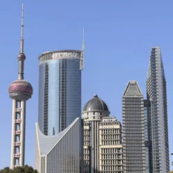 Shanghai skyline with the Oriental Pearl Tower and several modern high-rise buildings under a clear blue sky.